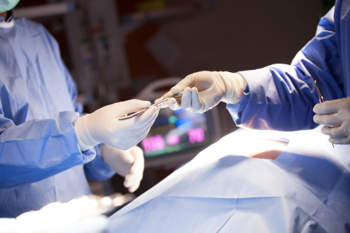 Patient on table covered in surgical draping in operating theatre while medical staff pass medical equipment to each other. Patient on table covered in surgical draping in operating theatre while medical staff pass medical equipment to each other.
