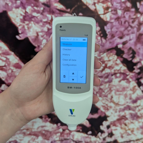 Hand holding jaundice meter with screen turned on against pink floral wallpaper background. Hand holding jaundice meter with screen turned on against pink floral wallpaper background.